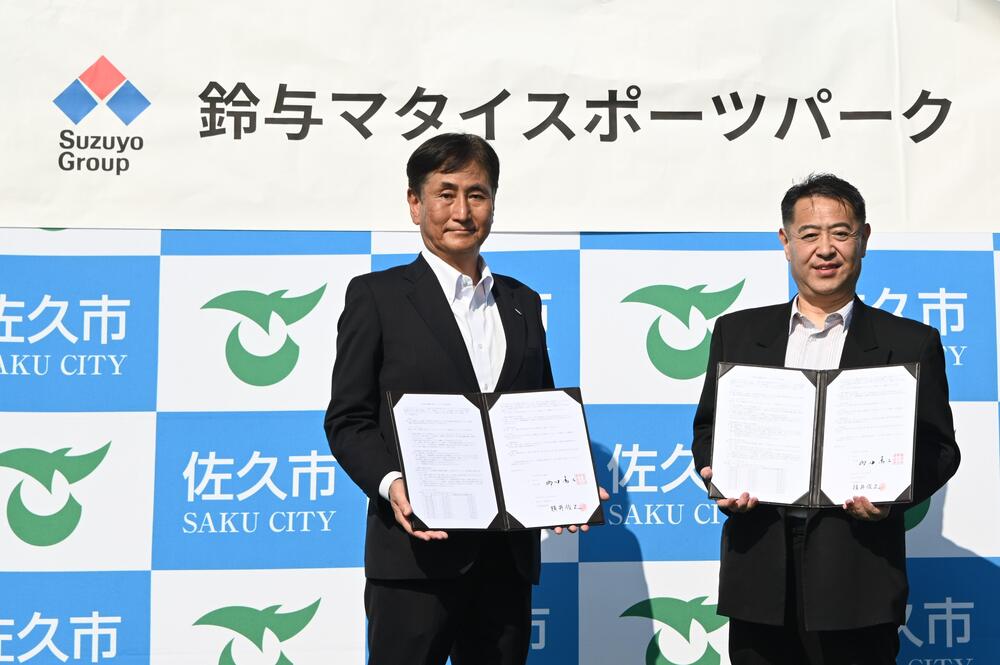 鈴与マタイスポーツパークの愛称を背景に協定書を持つ（左）鈴与マタイ株式会社社長横井俊之様、（右）佐久市長栁田清二